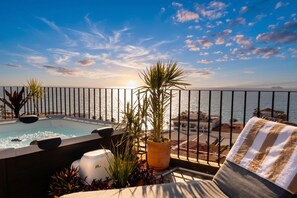 Une piscine sur le toit offrant une vue sur la mer, entourée de plantes en pot et agrémentée d’une serviette à rayures.