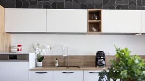 Una cocina moderna con armarios blancos, encimera de madera, lavaplatos integrado, cafetera y una orquídea en maceta.