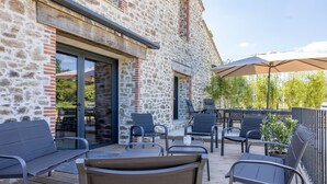 An outdoor patio with stone walls, a wooden deck, and outdoor furniture. - Le Domaine de la Haye - Group gîte for 16 people - 15 minutes from Puy du Fou (Saint-Christophe-du-Bois)