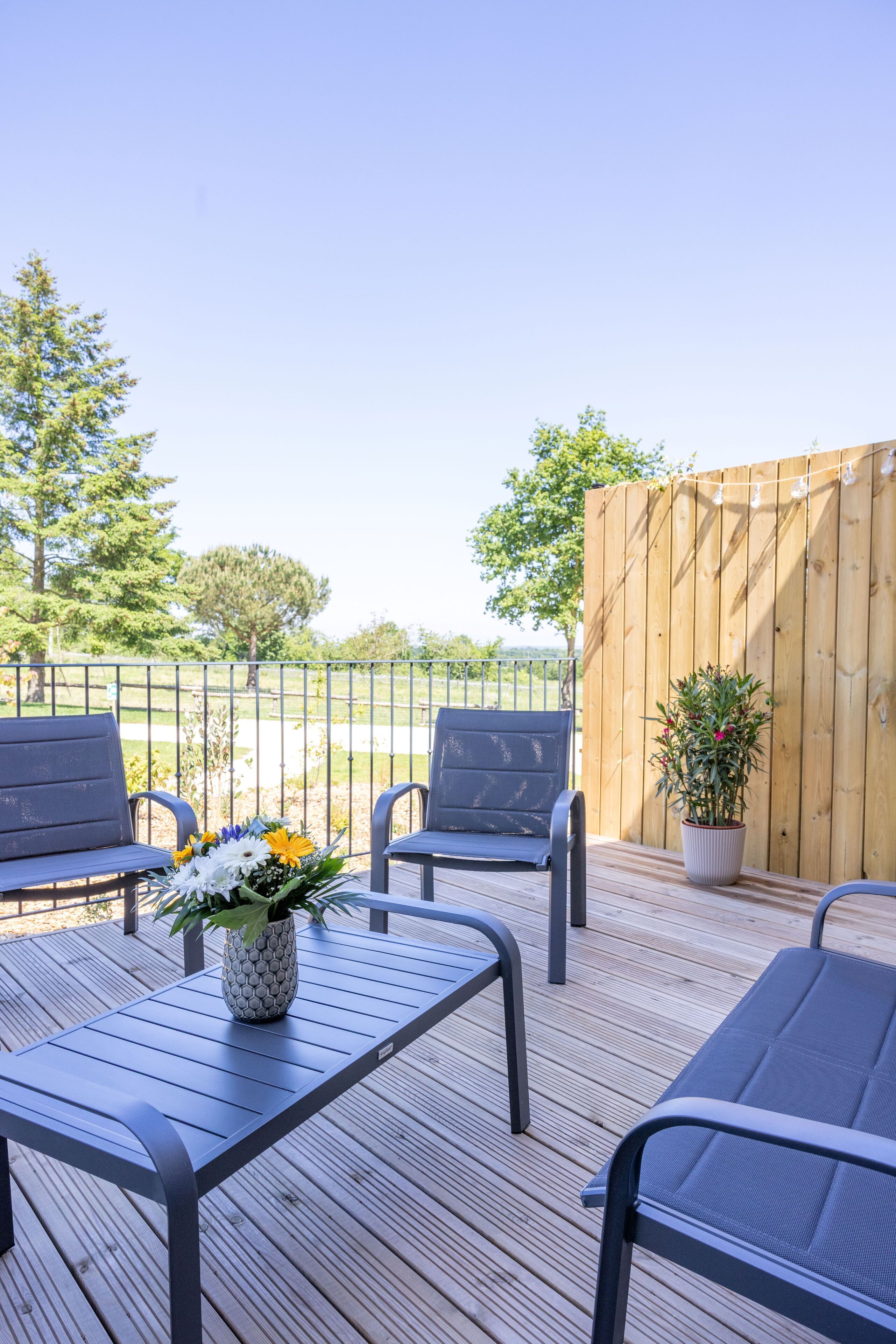 Une terrasse extérieure avec une plateforme en bois, des chaises en métal, une table et un pot de fleurs.