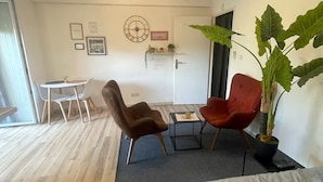 A modern room with a bed, two chairs, a small table, a potted plant, and a wall clock. - Superb studio in secure residence with swimming pool (Gagnac-sur-Garonne)