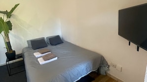 A neatly made bed with a grey bedspread, a potted plant, and a remote control on a bedside table. - Superb studio in secure residence with swimming pool (Gagnac-sur-Garonne)
