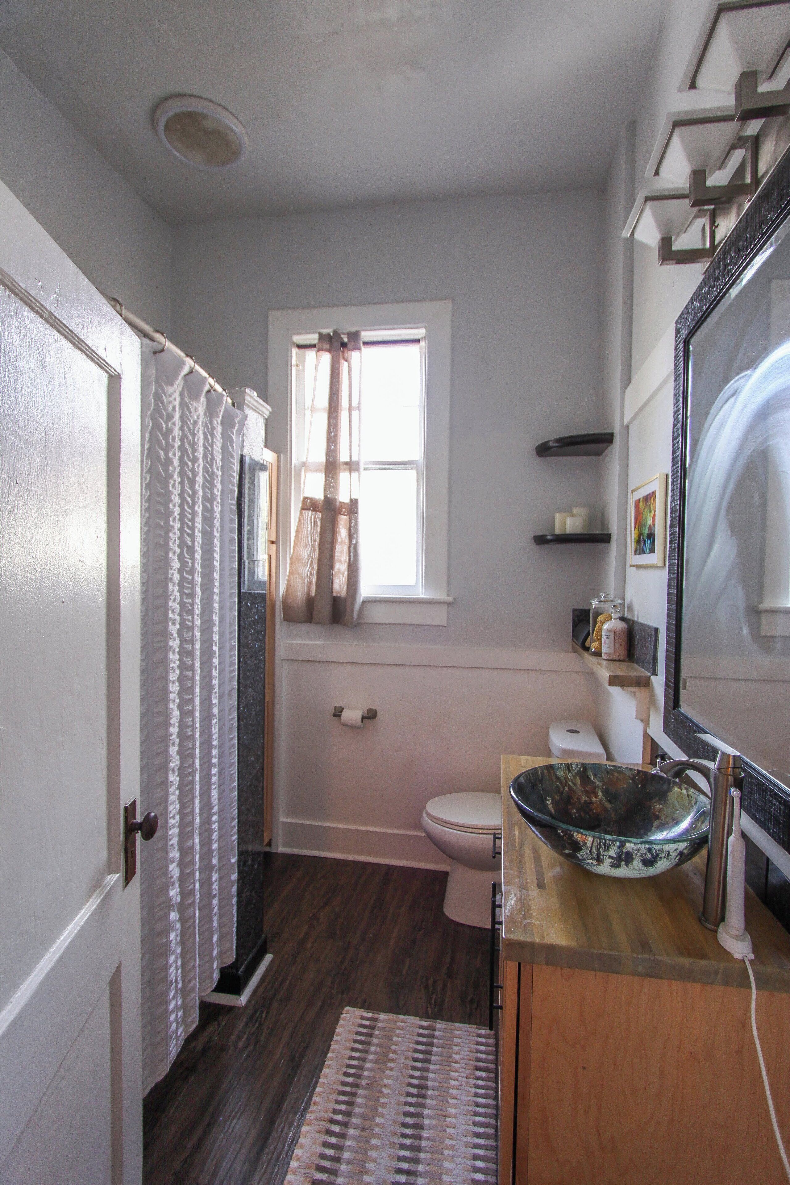 A bathroom with a toilet, a sink with a large bowl, a window with curtains, and a mirror.