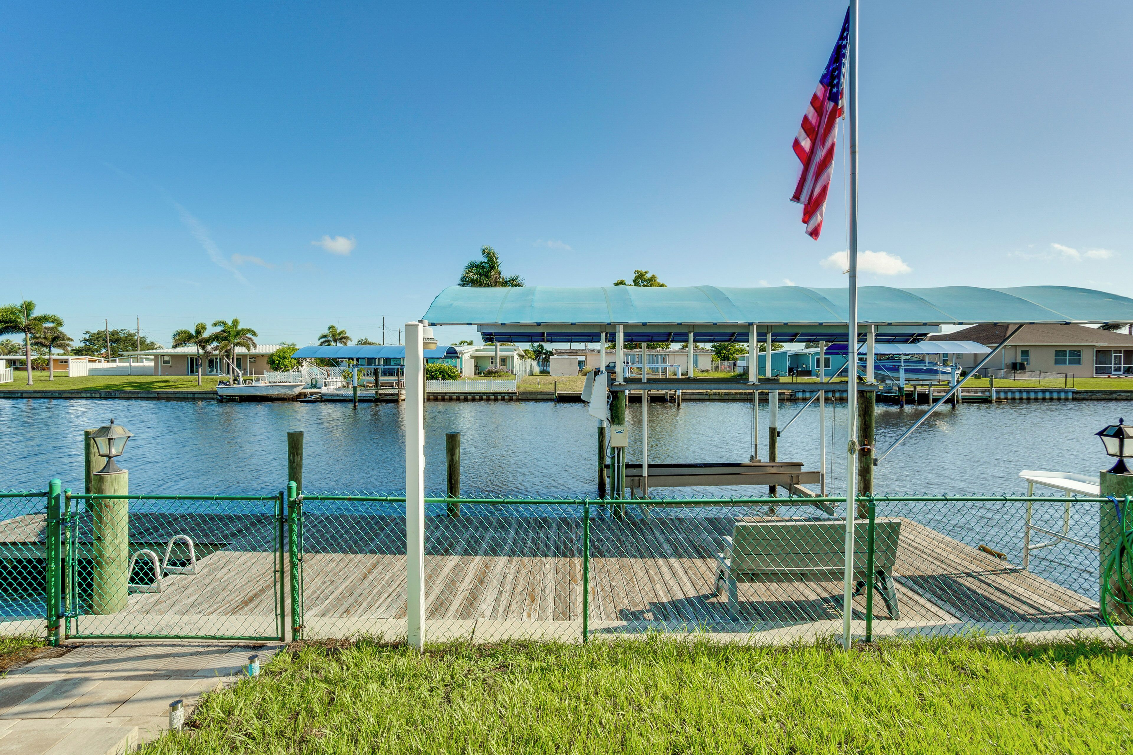 A waterfront dock with a covered seating area, a flagpole with an American flag, and a body of water.