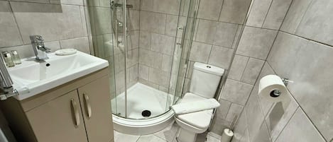 Casa de banho compacta com chuveiro em cabine de vidro, lavatório branco e sanita.