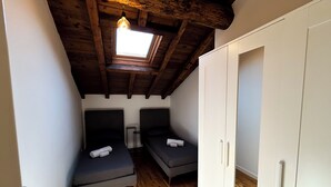 A small, narrow room with two single beds, a white wardrobe, and a skylight.