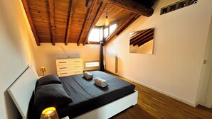 Ein Schlafzimmer mit Holzboden, einem Bett mit schwarzer Bettwäsche, einem weißen Nachttisch mit Lampe und einer Kommode.