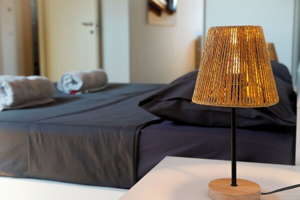 A bed with a dark-colored bedspread and pillows, a bedside table with a lamp, and a wall-mounted clock.