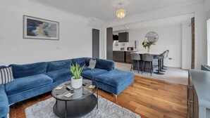 Ein modernes Wohnzimmer mit einem blauen Sofa, einem Couchtisch mit Pflanze und einer Küche im Hintergrund.