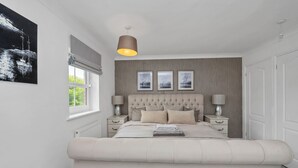 Ein Schlafzimmer mit einem großen Bett, Nachttischen, einer Pendelleuchte und drei gerahmten Bildern an der Wand.