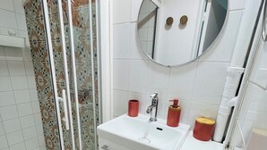 A bathroom with a glass shower enclosure, a white sink with a mirror above it, and a red towel on the counter. - Apartment triple gare Angers (Angers)