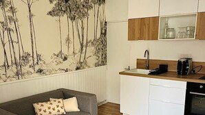 A modern living space with a grey sofa, a small round table, and a kitchen area with white cabinets and a coffee machine. - Apartment triple gare Angers (Angers)