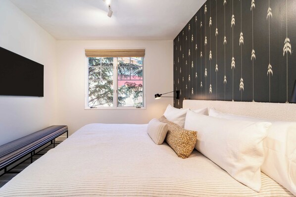 Un dormitorio con una cama grande, un banco, una ventana con vistas a árboles y una pared con un diseño.
