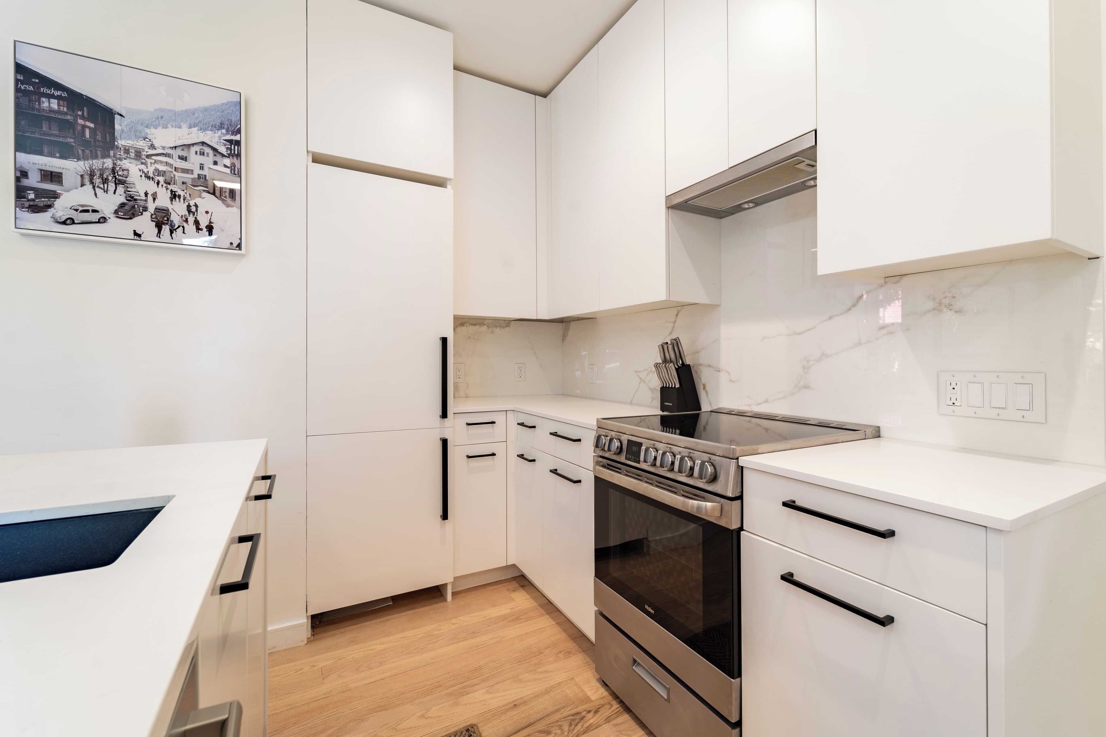 A modern kitchen with white cabinets, a stainless steel stove, and a marble backsplash.