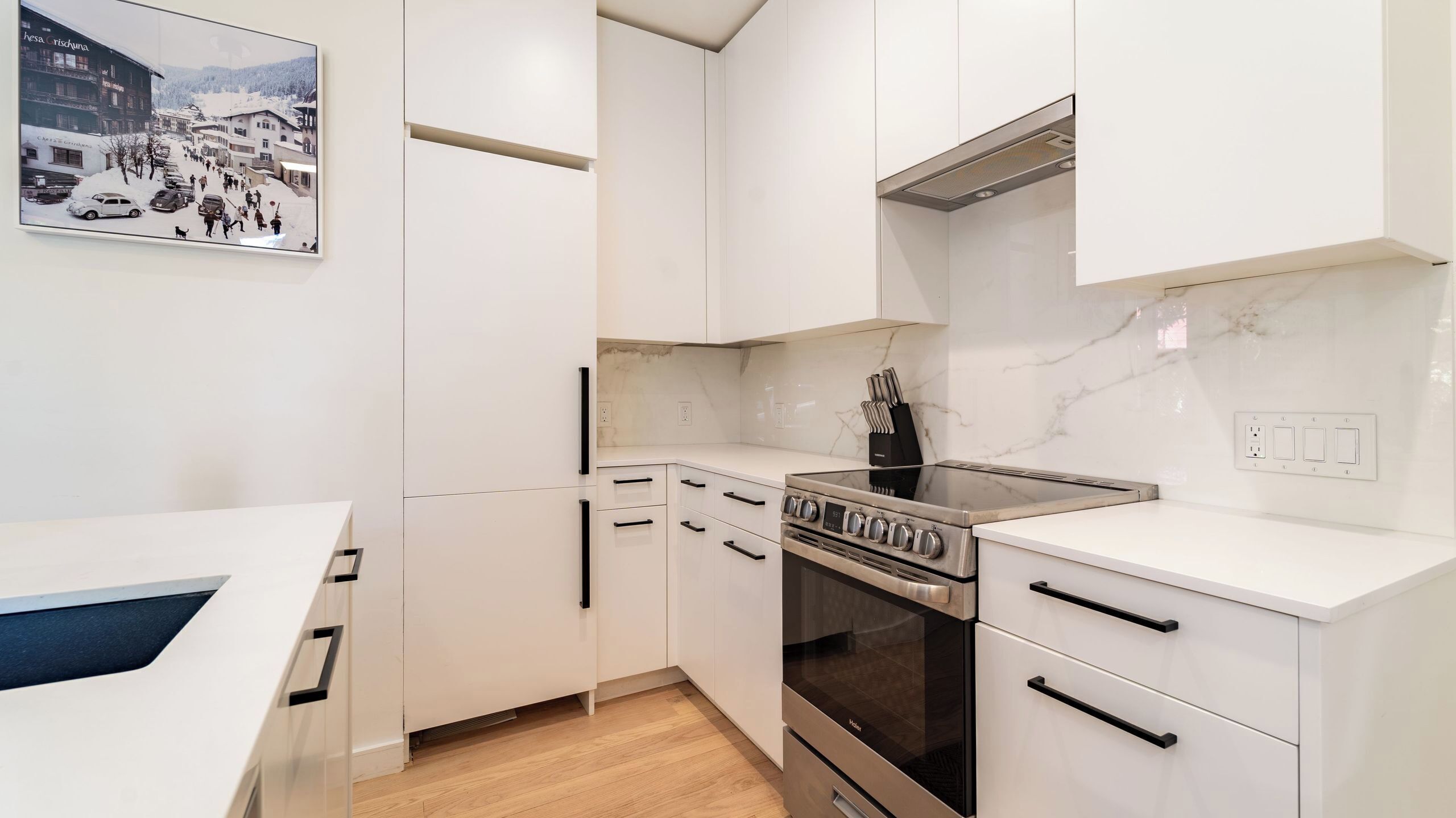 A modern kitchen with white cabinets, a stove, and a marble backsplash.
