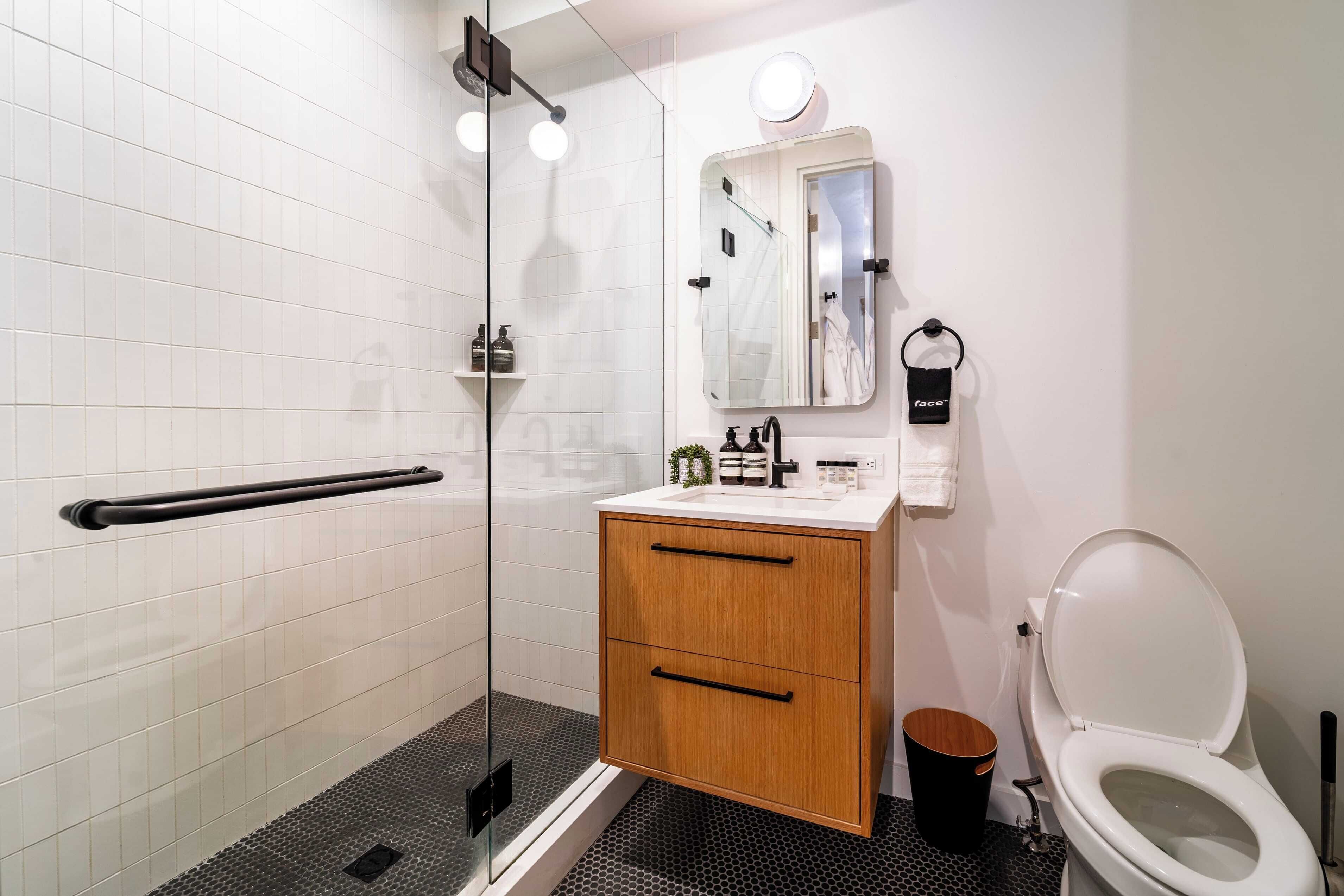 Un bany modern amb un plat de dutxa de vidre, un lavabo blanc amb un mirall damunt i un vàter blanc.