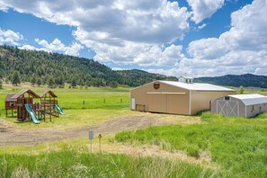 A large barn with a metal roof, a wooden play structure with a slide, and a fenced field. - Creekside Florrisant Hideaway - Great for Anglers! (Florissant)
