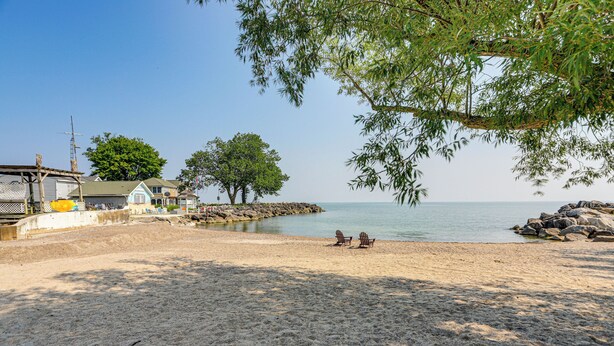 Una playa arenosa con dos sillas, un árbol y un edificio con techo azul.
