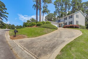 A residential driveway leading to a two-story house with a curved driveway, surrounded by well-maintained lawns and tall trees. - Pool & Tennis Court Access: Home in Warner Robins (Warner Robins)