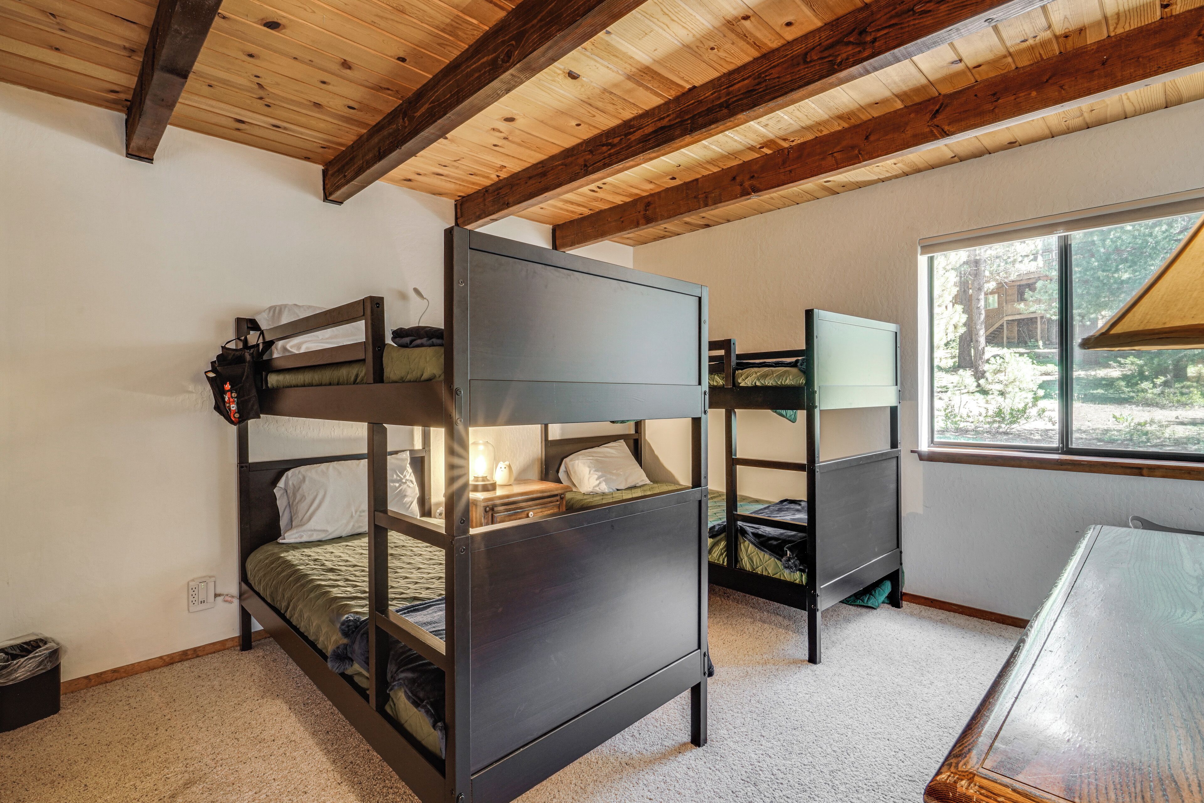 A bunk bed room with a wooden ceiling and a window providing a view of the outdoors.