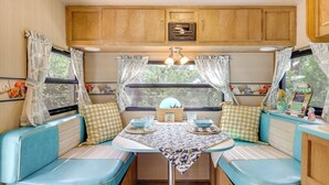 A cozy RV interior with a kitchenette, a dining area with a table and chairs, and a window with curtains. - 6 Mi to Wimberley Square: 'Happy Days Cruiser' (Wimberley)