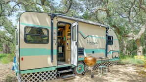 A vintage camper with an open door, a barbecue grill, and a dining table set up outside. - 6 Mi to Wimberley Square: 'Happy Days Cruiser' (Wimberley)
