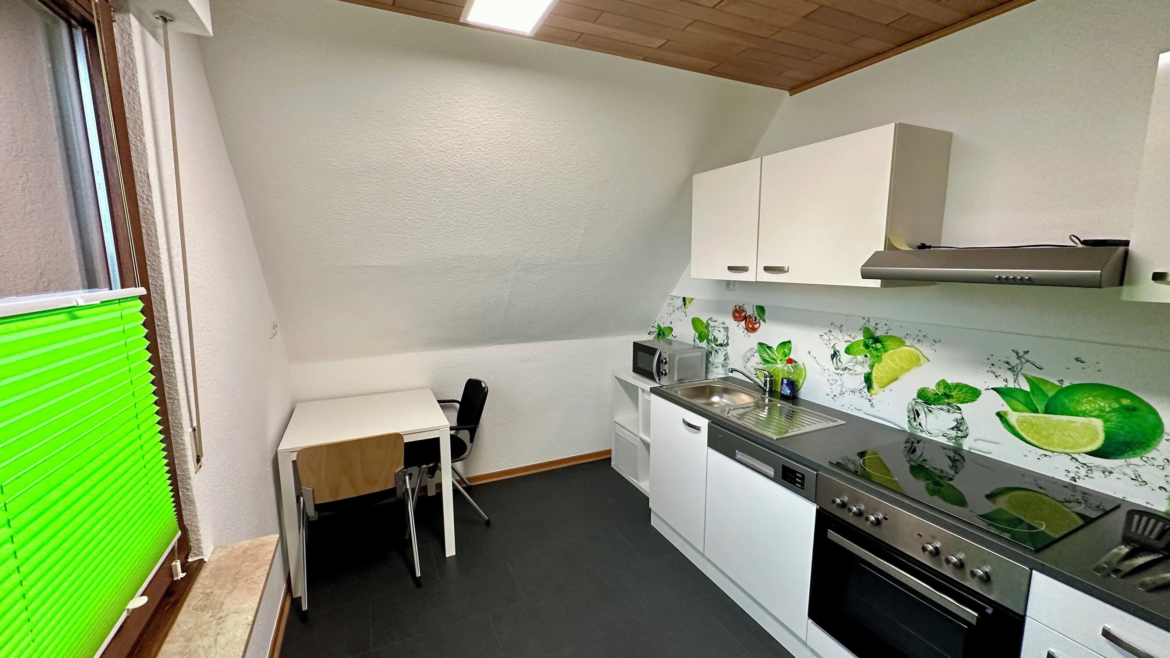 A compact kitchen with white cabinets, a microwave, a sink, and a tiled backsplash with a lime design.