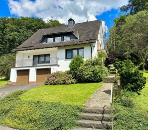 A two-story house with a tiled roof, a balcony, and a well-maintained garden. - Vacation Apartment with a View of the Naturarena (Reichshof)