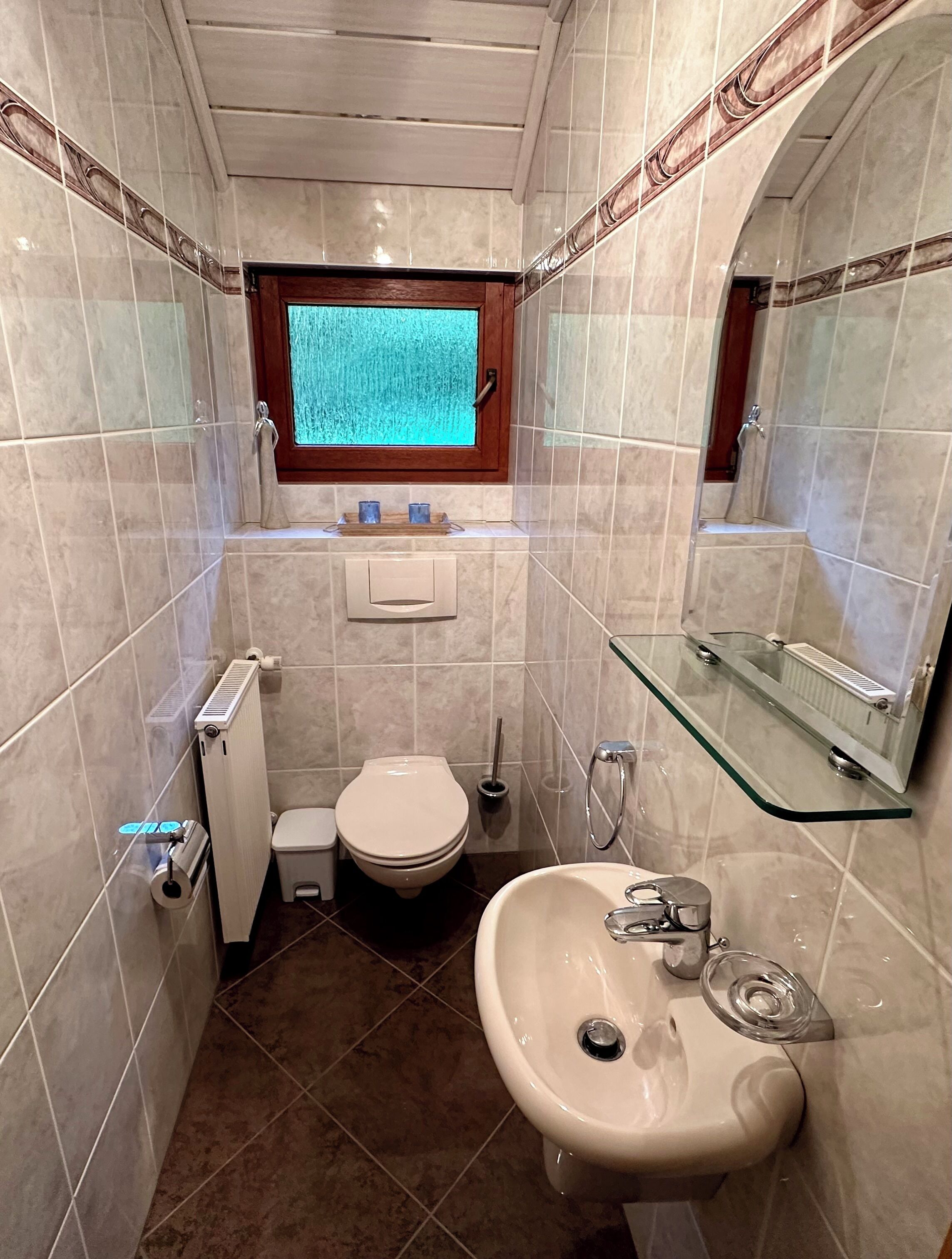 Une petite salle de bain comprenant des toilettes, un lavabo et une fenêtre située au-dessus des toilettes.