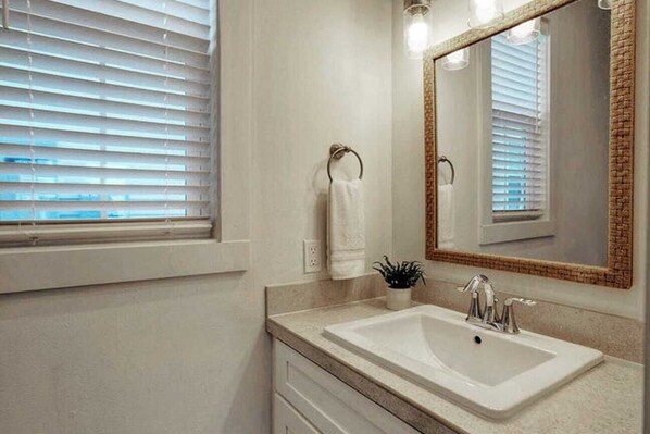 Un baño con un espejo grande, un lavamanos y una ventana con persianas.