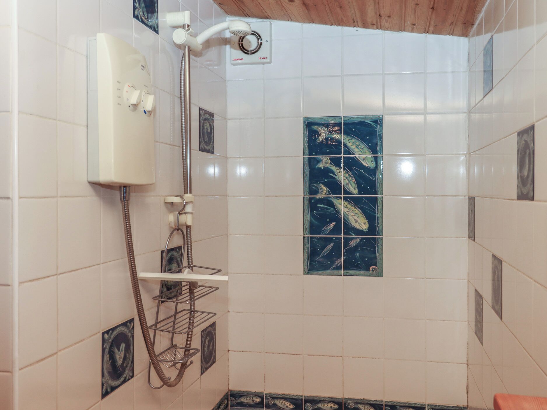 A shower with a white wall, a tiled showerhead, and a small shelf with a towel.