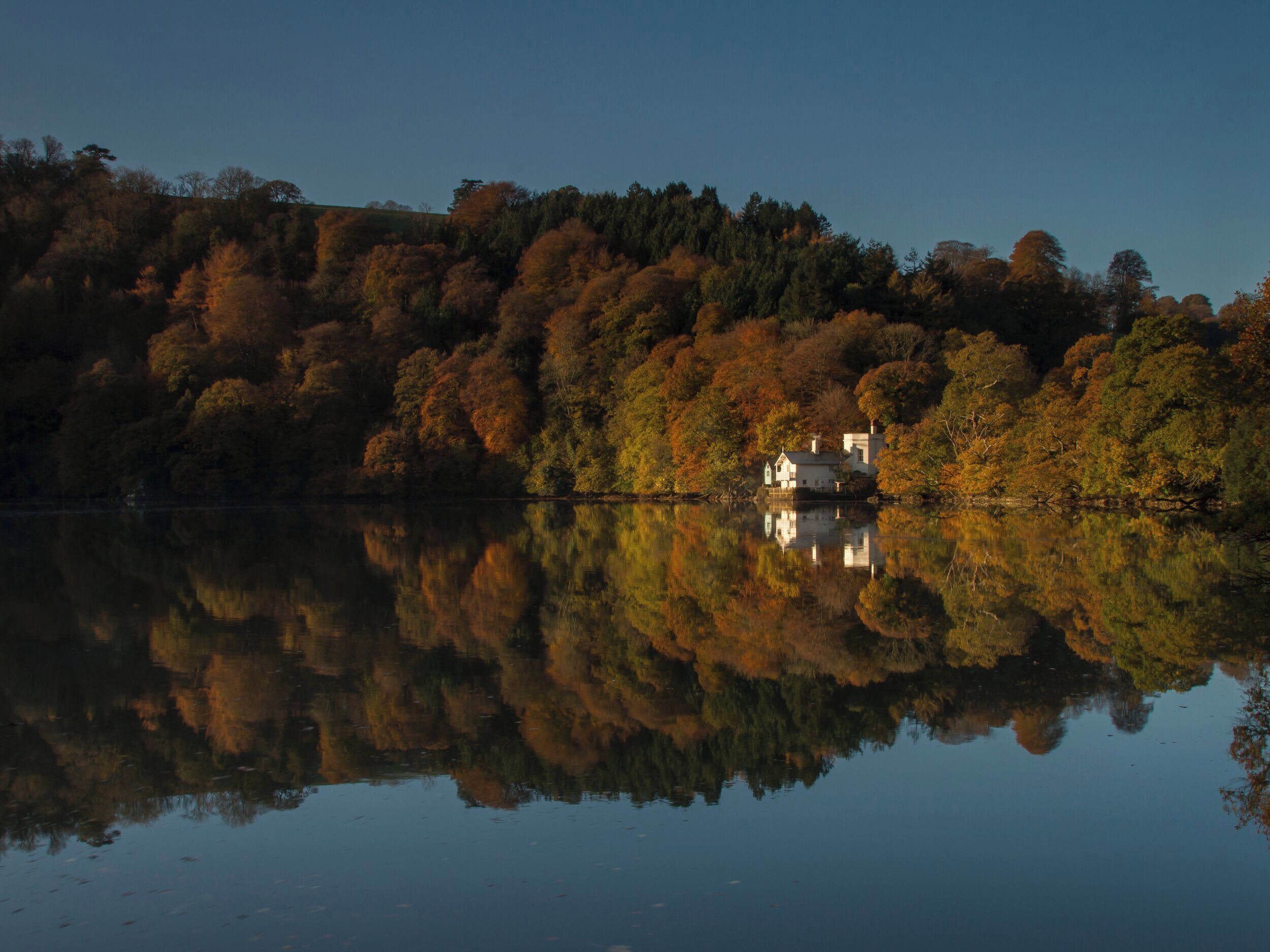 Een huis aan een rustig meer, met weerspiegelingen van bomen en het huis zelf.