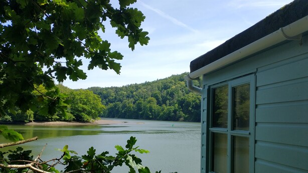 A cabin with a view of a calm lake and forested hills. - The Sharpham Boat House (Totnes)