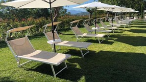 A row of outdoor lounge chairs with attached umbrellas, arranged on a well-maintained lawn. - IL POGGIO DEGLI ANTICHI SAPORI (Paternopoli)