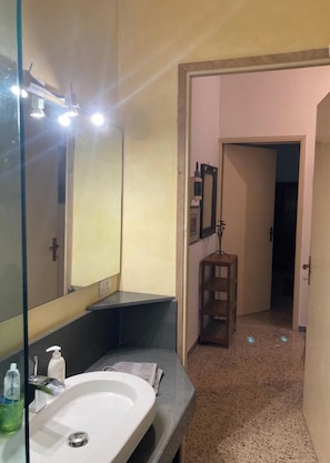 Un baño con lavamanos blanco, un espejo y una estantería con artículos de aseo.