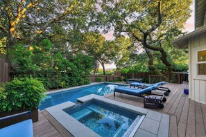 Une piscine entourée de chaises longues, de verdure luxuriante et d’une terrasse en bois.
