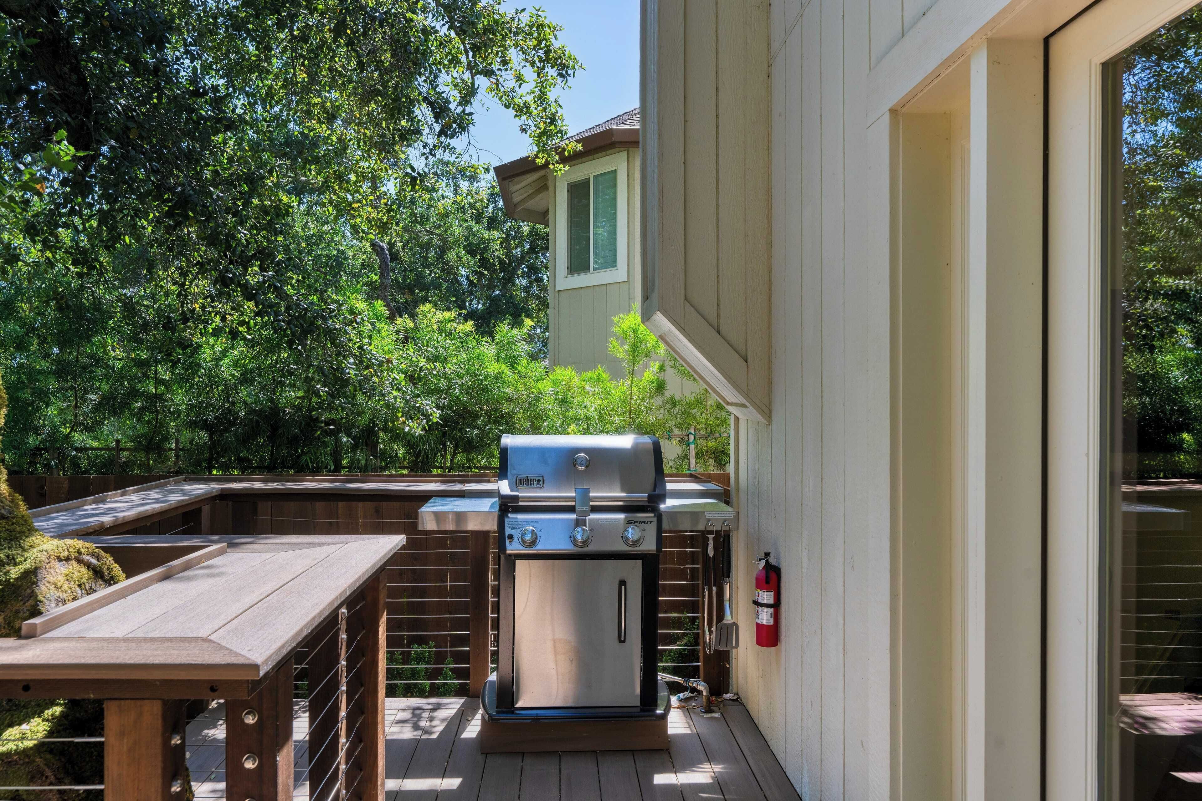 Ein Außenbereich mit Grillstation und Holztisch, umgeben von einer Holzterrasse und einer Ziegelmauer.