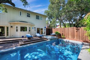 Une maison à deux étages avec une piscine, un espace salon extérieur et une clôture en bois.