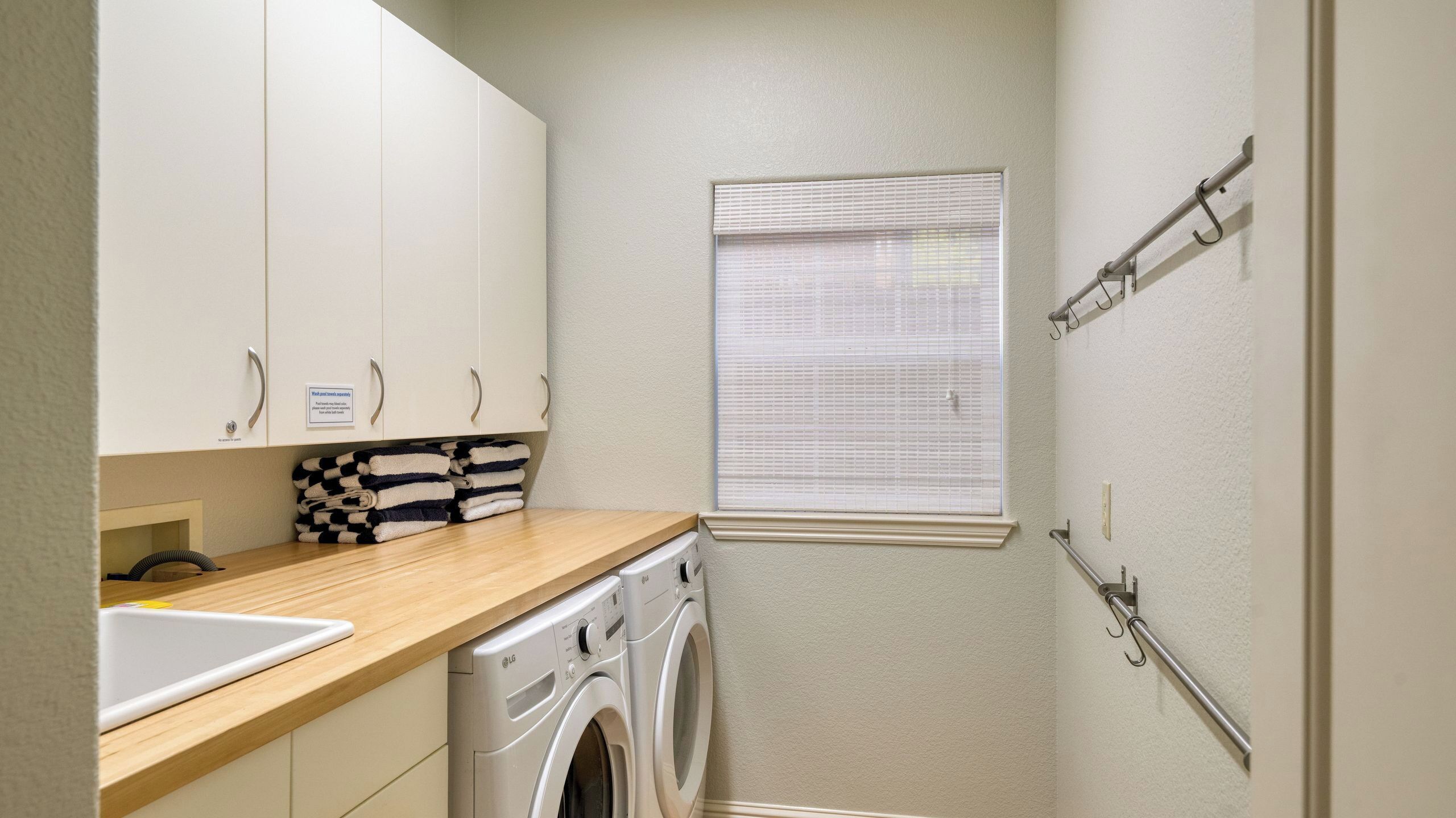 A compact laundry room with a washing machine, a sink, and a window with blinds.