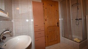 Une salle de bain avec un lavabo blanc, une porte en bois et une douche fermée par des parois de verre.