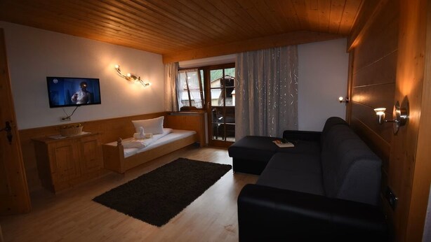 Un salon chaleureux avec un plafond en bois, un téléviseur à écran plat fixé au mur, un canapé, une petite table avec un panier et un tapis noir.