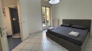 Une chambre avec un grand lit, une porte donnant sur une salle de bain et une fenêtre offrant une vue sur la verdure.