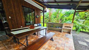 Un espace de restauration en plein air avec une table et des bancs en bois, un four en briques et une vue sur une végétation luxuriante.
