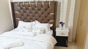 A neatly made bed with white bedding, a tufted headboard, and a small bedside table with a vase of flowers. - one bedroom apartment in juja (Juja)
