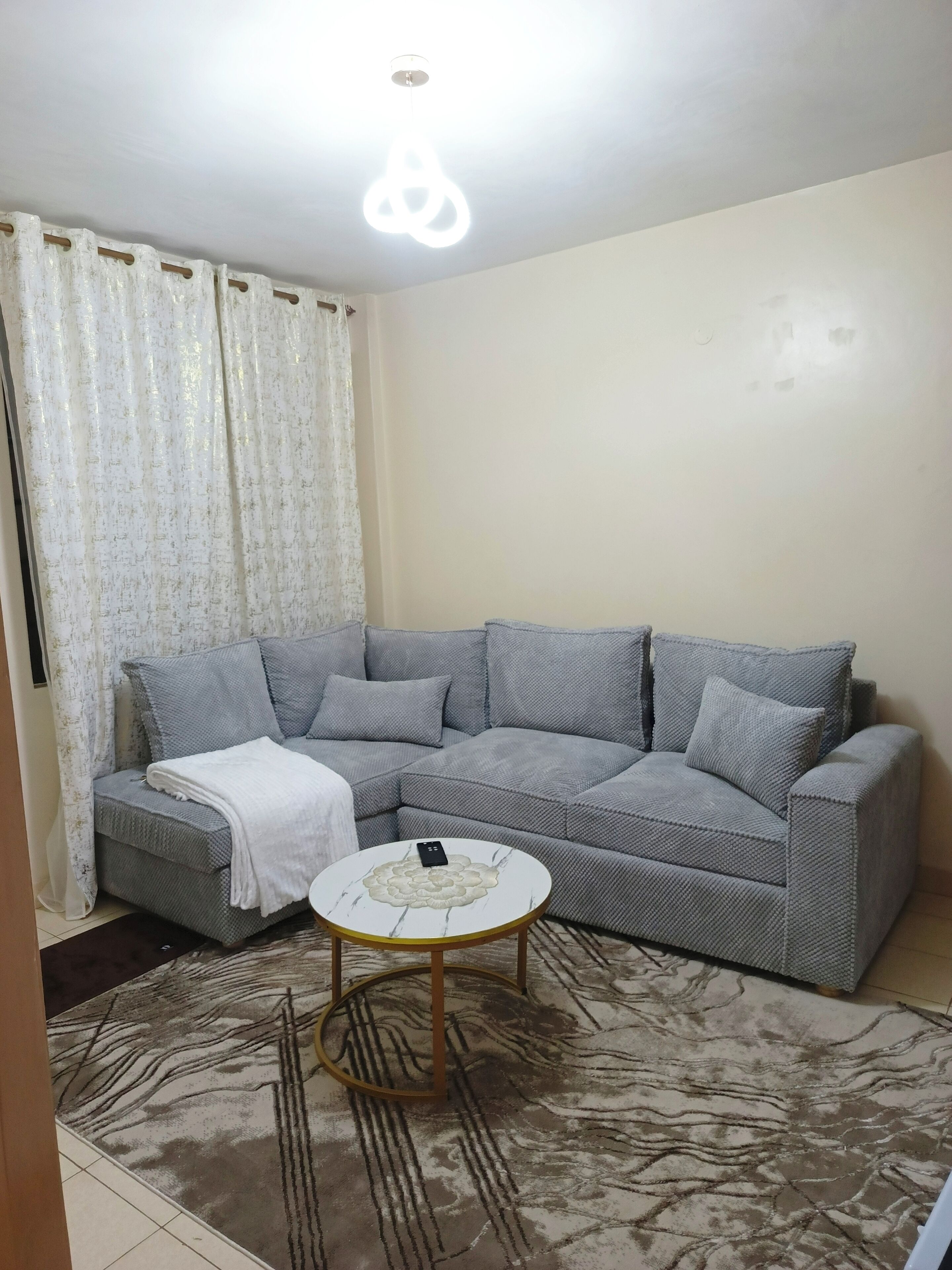 A living room with a grey sofa, a white throw blanket, a round coffee table, and a patterned rug.