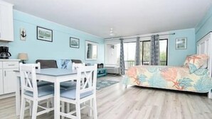 Una habitación con una mesa de comedor, sillas, una cama con edredón estampado y una ventana con cortinas.