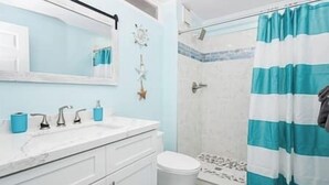 Un baño con un lavabo blanco, un espejo, una ducha con cortina azul y blanca, y un inodoro.