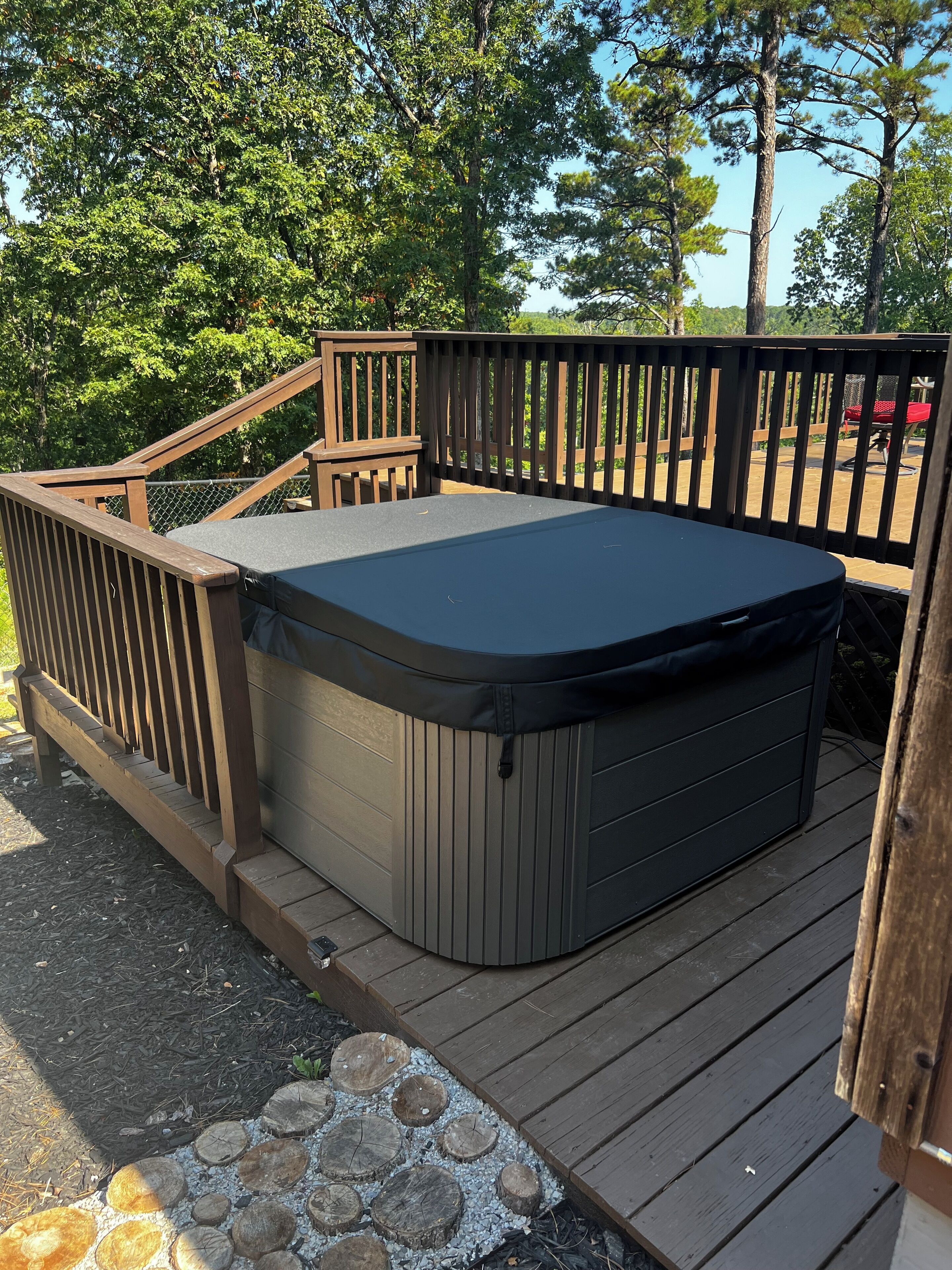 Un jacuzzi en una terraza de madera con barandilla, rodeado de árboles.