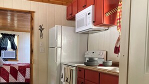 Cocina compacta con refrigerador, estufa, microondas y gabinetes rojos.