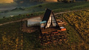 Une maison avec un toit en pente et une extension en verre, entourée d’une propriété clôturée où l’on peut apercevoir des chevaux qui paissent au loin.